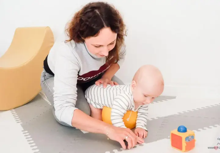 Mama wspiera 2-miesięczne dziecko w pierwszych próbach raczkowania. Zabawy z maluszkiem na macie.