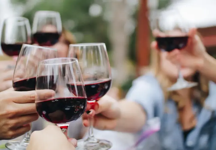 Des mains portent des verres de vin rouge pour un toast. Un moment convivial autour d'un vin doux apéritif.