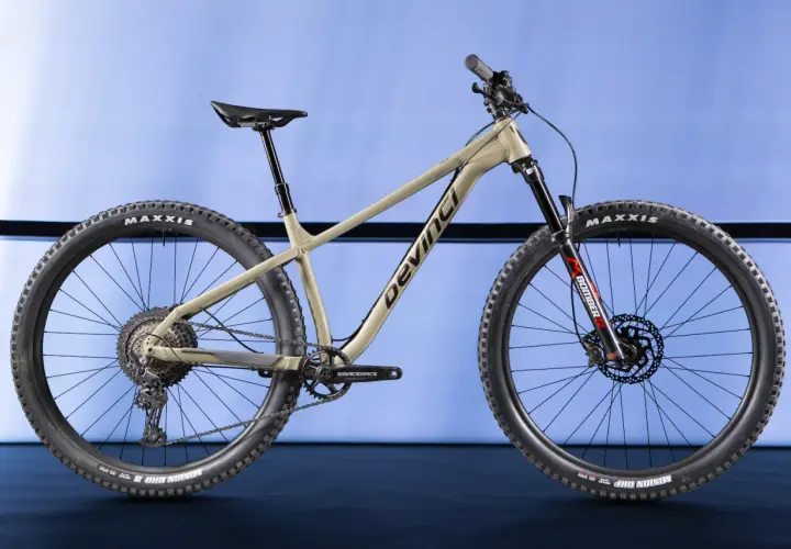 A tan Devinci Kobain mountain bike with Maxxis tires and a Marzocchi Bomber fork, ready for any trail.