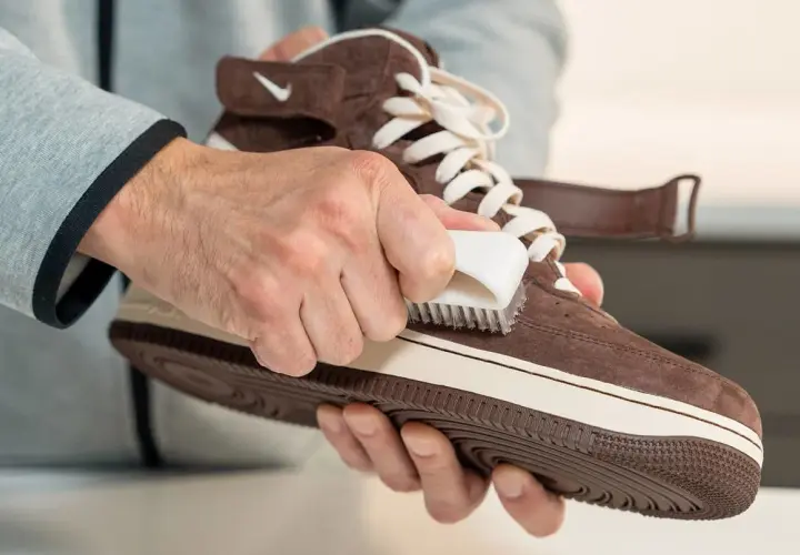 Man limpiando zapatillas de ante marrón con un cepillo blanco. Paso a paso para saber como limpiar zapatillas de ante y dejarlas como nuevas.