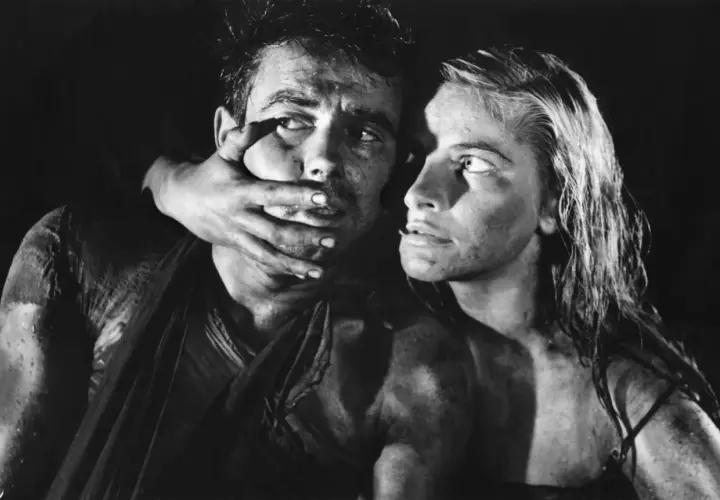 Dramatyczna scena z filmu Andrzeja Wajdy. Kobieta zakrywa usta mężczyźnie, ich twarze są spocone i brudne.