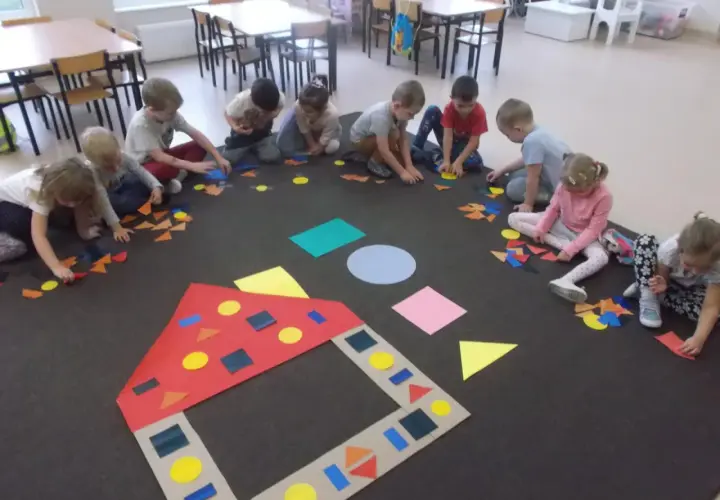 Dzieci w przedszkolu tworzą obrazki z kolorowych figur geometrycznych.
