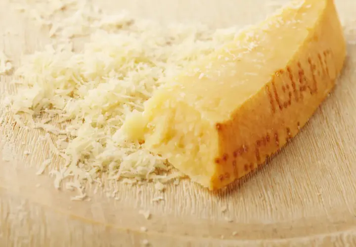 Ein Stück Parmesan mit geriebenem Käse daneben. Die Rinde ist deutlich geprägt und zeigt, dass die **Parmesanrinde essbar** ist.