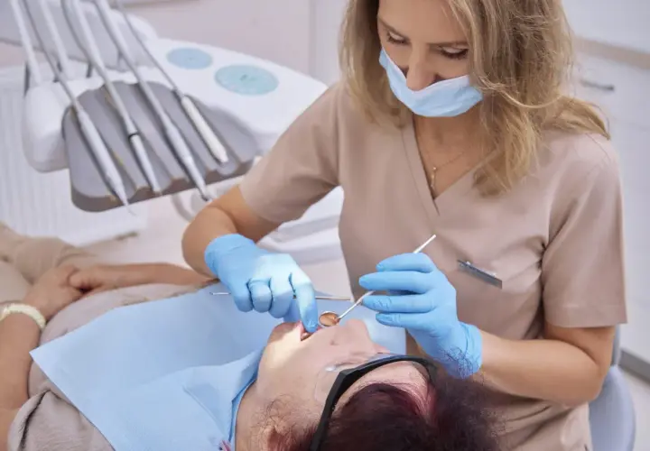 Dentystka bada pacjentkę, która skarży się na krwawiące dziąsła. W gabinecie stomatologicznym widać narzędzia dentystyczne.