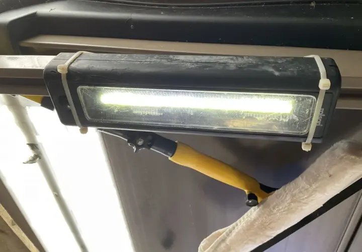 Jasne, oto opis:

Oświetlenie garażu bez prądu: prowizoryczna lampa LED na opaskach zaciskowych, oświetlająca wnętrze. Obok wisi narzędzie do czyszczenia.
