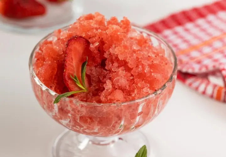 Sorbet truskawkowy w pucharku, ozdobiony plasterkiem truskawki i miętą.