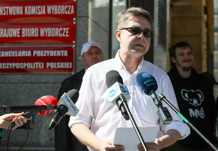 Mężczyzna przemawia do mediów przed budynkiem z napisem "Kancelaria Prezydenta RP". Dyskutuje się, dlaczego Pałac Prezydencki został wyłączony z części audytów dotyczących lotów państwowych.