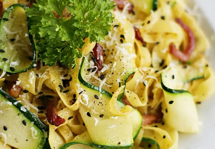 Pyszny makaron z cukinią i boczkiem, posypany parmezanem i czarnym sezamem, udekorowany natką pietruszki.