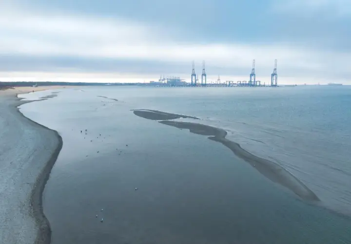 Plaża i morze z widocznym odpływem. W oddali port z dźwigami.