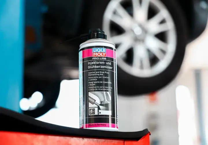 Puszka preparatu do czyszczenia wtryskiwaczy Liqui Moly na tle koła samochodu. Pomaga w demontażu zapieczonych elementów.