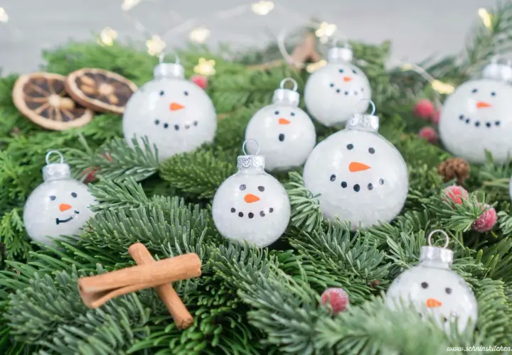 Schneemann-Weihnachtskugeln bemalen: süße Ideen für DIY-Deko. Tannengrün, Zimtstangen und getrocknete Orangen ergänzen die winterliche Szene.