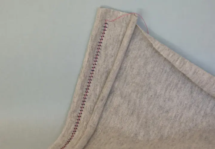 A close-up shows a grey fabric hem stitched with a twin needle, creating a decorative zigzag pattern.