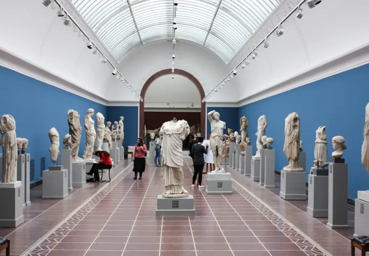 Wnętrze muzeum z rzeźbami antycznymi. Wśród zwiedzających artystka szkicująca posąg. Warto odwiedzić muzea w Krakowie.