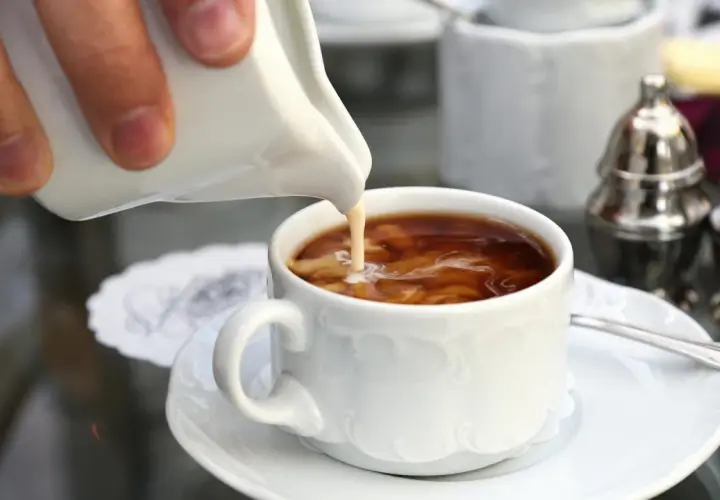 Ein Schwall Milch fließt in eine Tasse filterkaffee mit milchschaum. Ein Moment der Ruhe vor dem ersten Schluck.
