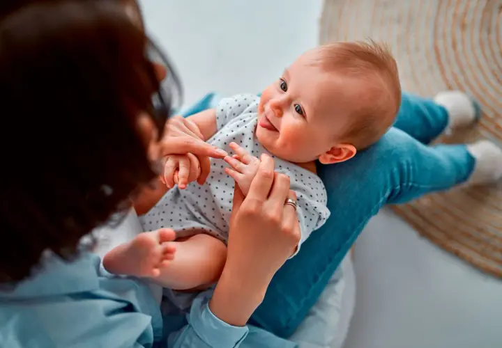 Madre juega con su bebé, enseñándole sus deditos. El bebé sonríe, quizás practicando sus primeras palabras.