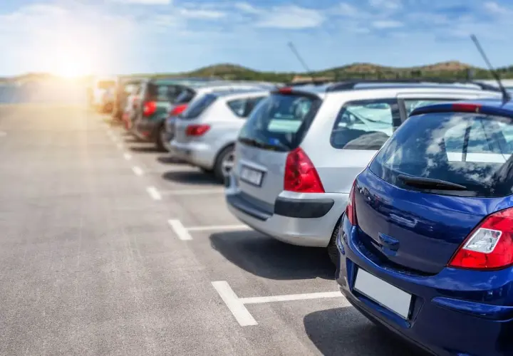 Rząd zaparkowanych samochodów na parkingu, z niebieskim samochodem na pierwszym planie.