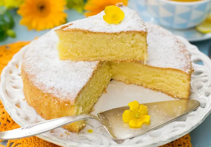 Una torta paradiso sofficissima, spolverata di zucchero a velo e decorata con un fiore giallo, pronta per essere gustata.