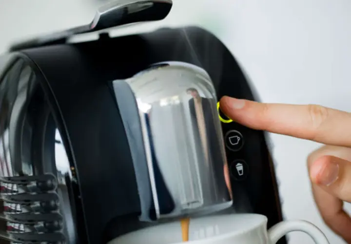 Finger drückt Knopf an Kaffeemaschine. Zeit, den Kaffeeautomaten zu entkalken für perfekten Kaffeegenuss.