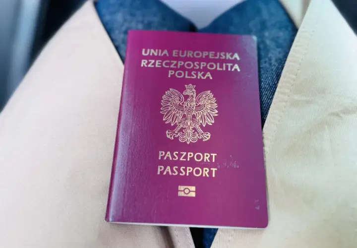 Polski paszport leżący na jasnym płaszczu i dżinsach.