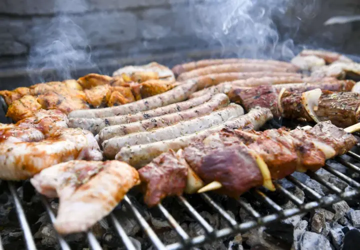 Des saucisses, brochettes de viande et morceaux de poulet à faire un barbecue sur un gril chaud, avec de la fumée qui s'échappe.