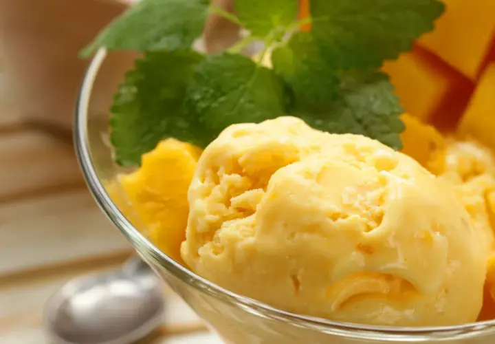 Domowe lody mango z miętą w szklanej miseczce.
