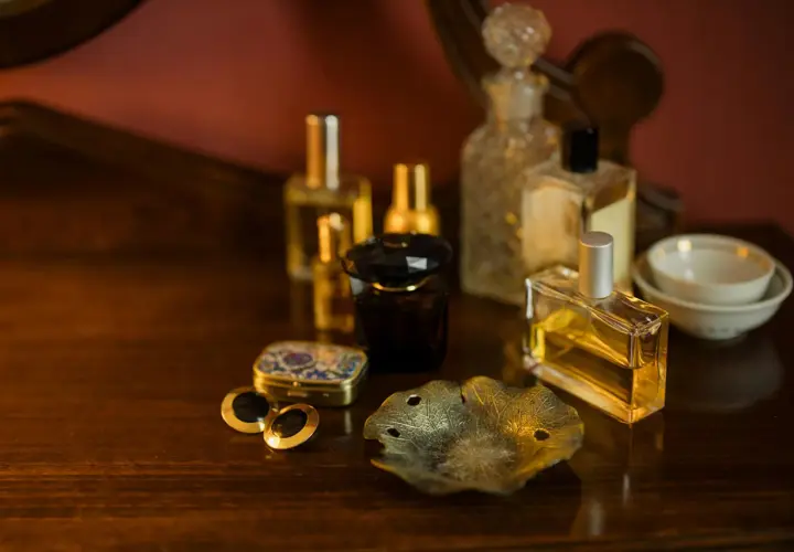 Eleganckie flakoniki z perfumami i woda kolońska co to? Na drewnianym blacie stoją różne rodzaje perfum, spinki do mankietów i ozdobna szkatułka.