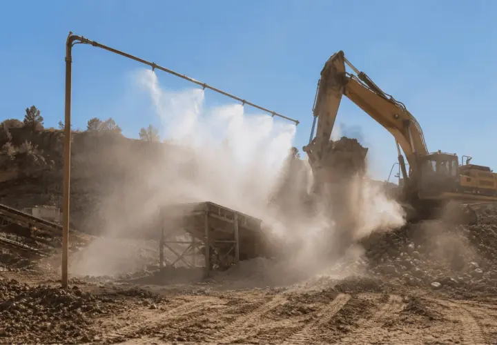Excavadora amarilla trabajando en cantera, con sistema de desinfección por nebulización para controlar el polvo.