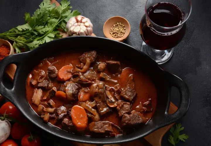 Un plat de bœuf bourguignon mijoté, avec carottes, champignons et oignons, accompagné d'un verre de vin pour bourguignon.