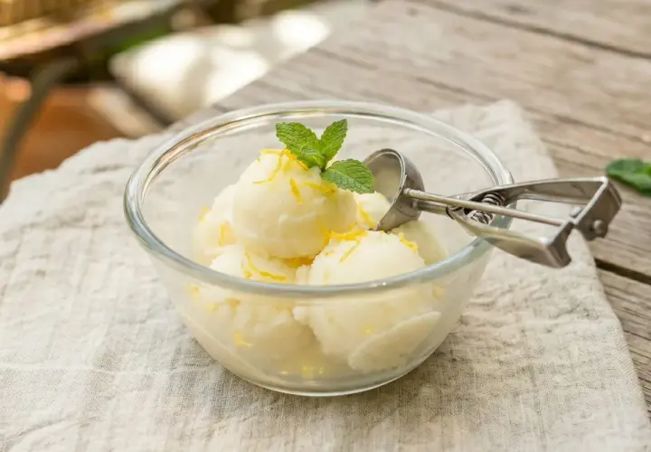 Un délicieux sorbet citron sans sorbetière, garni de menthe fraîche et de zestes de citron, servi dans un bol en verre.