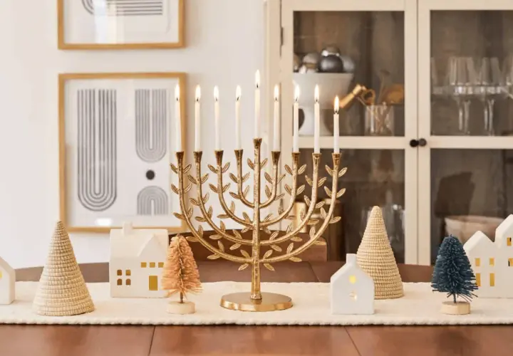 A golden menorah with lit candles is the centerpiece of this Chanukah decorating idea, surrounded by miniature houses and trees.