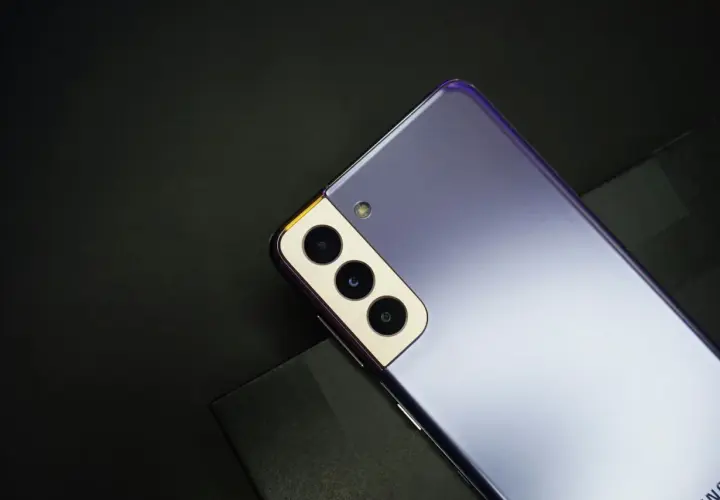 Fioletowy Samsung S21, rok produkcji 2021, z potrójnym aparatem i złotą ramką, leży na czarnym tle.