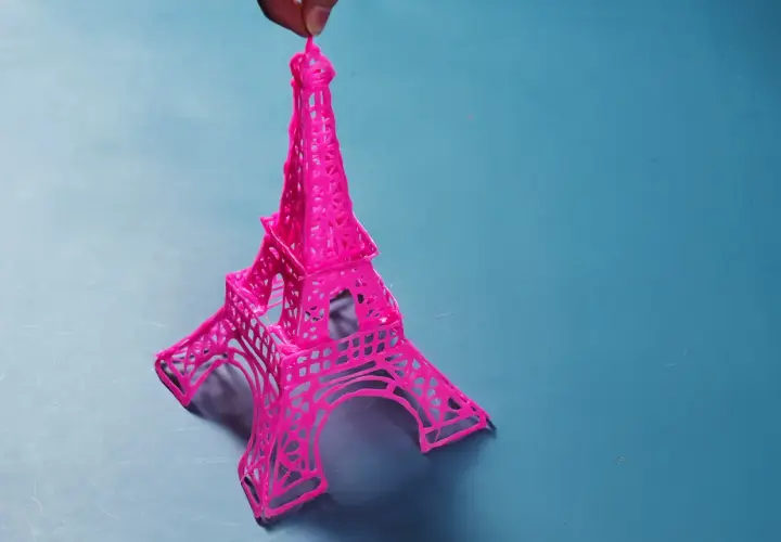 Una manualidad de la Torre Eiffel rosa, creada con filamento, sostenida por un dedo.
