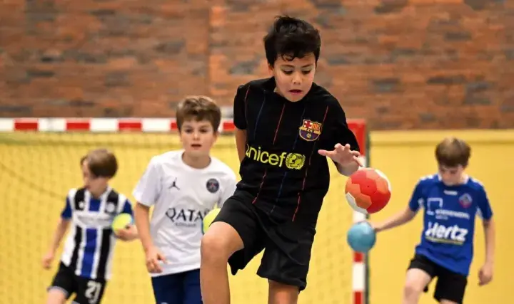 Jungen in Sporttrikots spielen Staffelspiele mit Ball in einer Sporthalle.