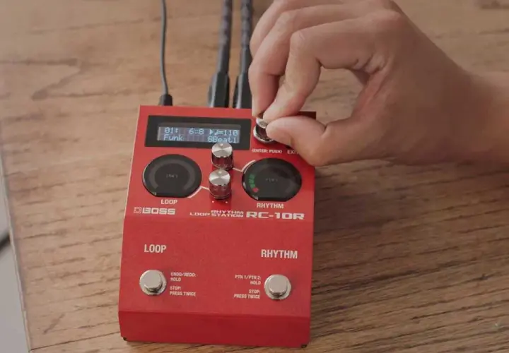 Dłoń kręci gałką na czerwonym looperze do gitary Boss RC-10R, ustawiając rytm funk.