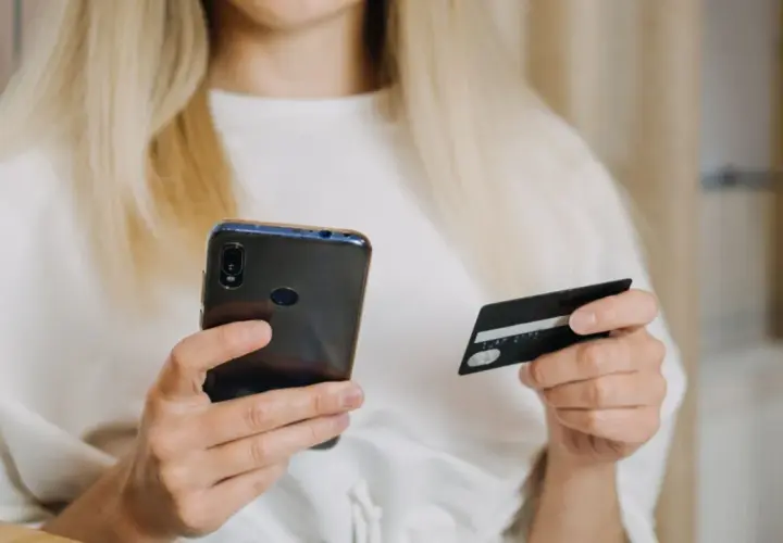 Kobieta z blond włosami trzyma telefon i kartę płatniczą, szukając informacji, jak zwiekszyc limit PayPo.