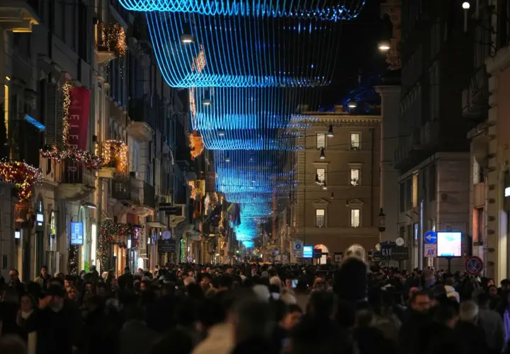 Folla festosa in strada a Roma, 25 dicembre, sotto luminarie blu e decorazioni natalizie.