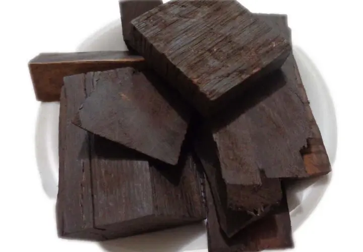 Pezzi di legno scuro, forse ebano, il legno più costoso del mondo, su un piatto bianco.