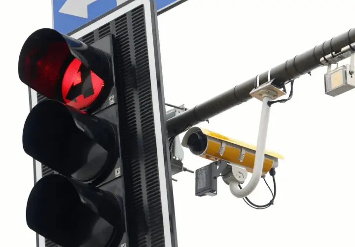 Czerwone światło sygnalizacji świetlnej z zakazem skrętu w lewo. Obok zamontowana kamera monitorująca.