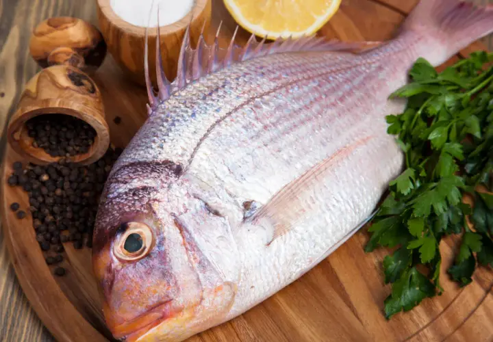 Un pescado rojo, listo para cocinar con perejil, limón, sal y pimienta negra.