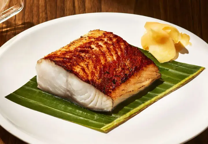 A perfectly seared Nobu miso black cod recipe, served on a banana leaf with pickled ginger.