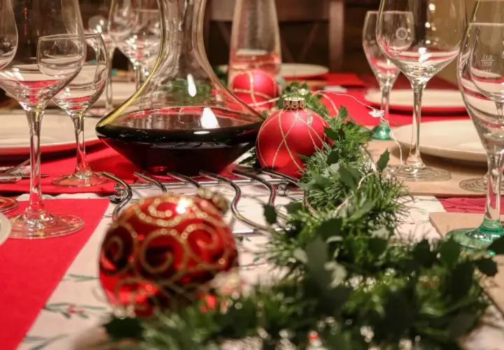 Table dressée pour Noël avec carafe de vin rouge. Combien de cubi de vin pour 40 personnes ? Boules rouges et guirlande verte.