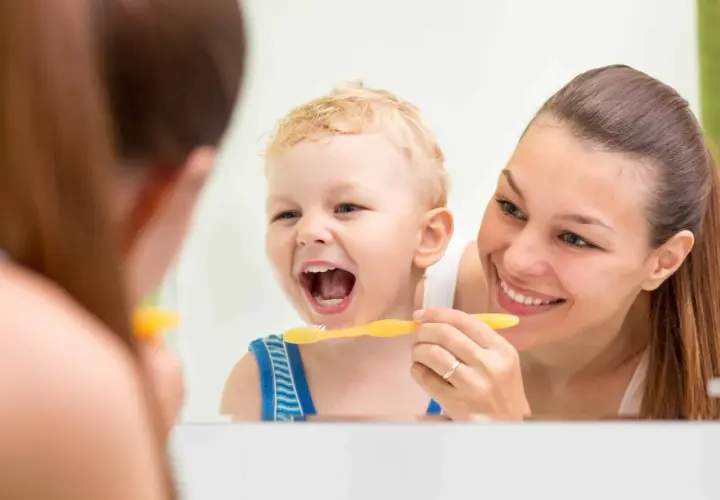 Mama uczy malucha, jak nauczyć dziecko myć zęby. Uśmiechnięty chłopiec z otwartymi ustami i żółtą szczoteczką.
