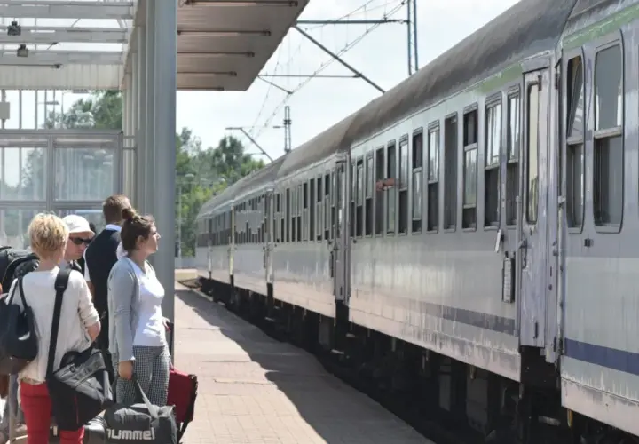 Ludzie z bagażami czekają na pociąg PKP. Zastanawiasz się, kto ma zniżki na PKP? Sprawdź ofertę przewoźnika!