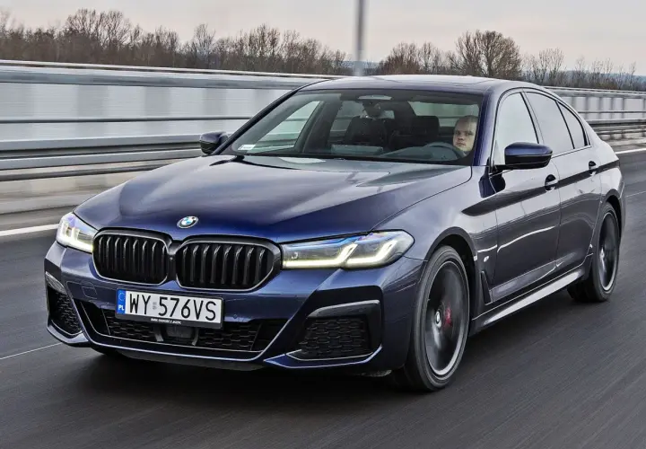 Ciemnoniebieskie BMW 520d xDrive jedzie autostradą. Kierowca z zaciekawieniem obserwuje drogę.