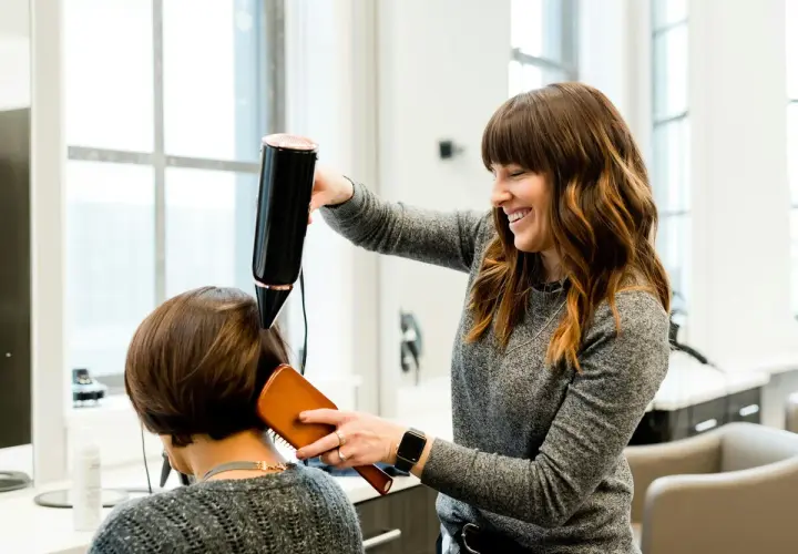 Estilista sonríe mientras seca el cabello de una clienta. Un buen momento para cortarse el pelo es cuando te sientes renovada.