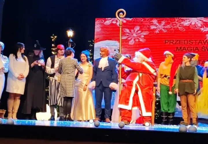 Aktorzy w strojach świątecznych i bajkowych na scenie, w tym Święty Mikołaj.