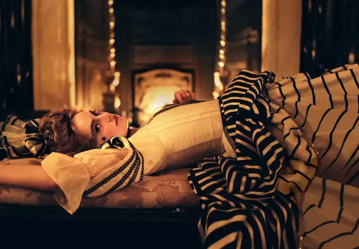 La favorita recensione: una donna con un abito a righe giace su un divano, illuminata da luci soffuse.