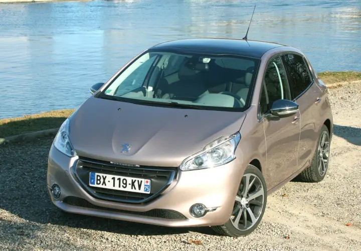 Peugeot 208 GPL color bronzo, parcheggiata su ghiaia vicino a un lago.