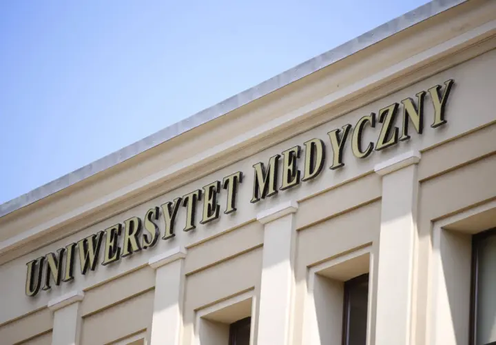Napis "Uniwersytet Medyczny" na jasnej fasadzie budynku pod błękitnym niebem.
