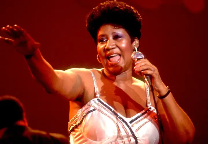 Aretha Franklin śpiewa na scenie, trzymając mikrofon. Jej dzieci z pewnością byłyby dumne z jej występu.